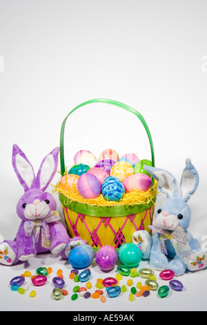 Straw Easter basket filled with colored eggs with stuffed easter bunnies and colorful candies Stock Photo