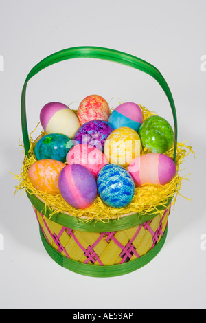 Straw Easter basket filled with a dozen colored eggs of different bright colors and patterns on a white background Stock Photo