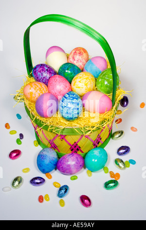 Straw Easter basket filled with eggs of different colors and patterns with candies spilling over Stock Photo