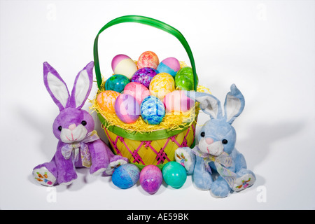 Straw Easter basket filled with eggs of different colors and patterns with two stuffed bunnies on either side Stock Photo