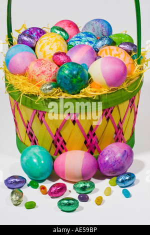 Easter basket filled with coloured eggs and chocolate candies in straw Stock Photo