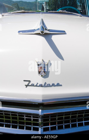 Front hood of a white 1955 Ford Fairlane classic car with emblem hood ornament grille and windshield Stock Photo