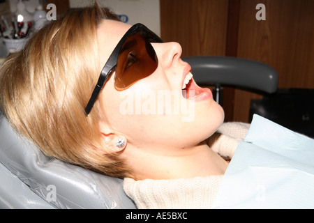 Pretty blonde young woman in dental chair protective glasses mouth wide open waiting for inspection by dental surgeon Stock Photo