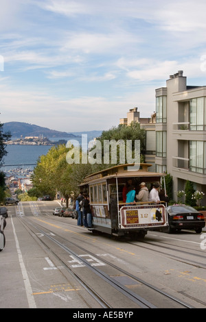 Cable car with tourists descending Hyde Street toward Fishermans Wharf with Alcatraz Island across  San Francisco Bay Stock Photo