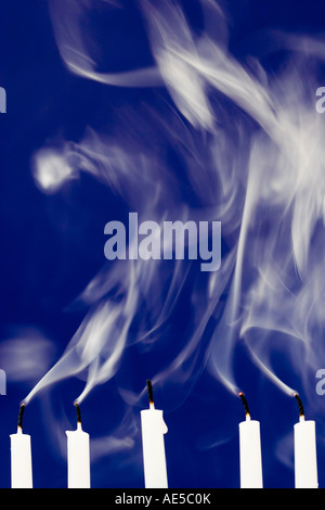 Five white candles against blue background with smoke rising after their flames were blown out Stock Photo