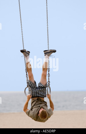 Man hanging upside down playing on rings set on Santa Monica Beach California Stock Photo
