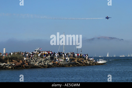 Crowd standing on promontory in San Francisco Marina district watching one of Blue Angels fly by as fog rises from water Stock Photo