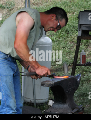 Farrier making a horseshoe by pounding red hot metal with a hammer on an anvil Stock Photo