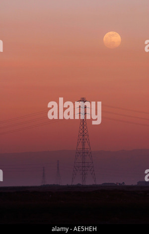 Moon rising over the silhouette of power towers and power lines against a pink sunset sky Redwood City California Stock Photo