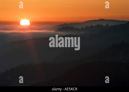 Sun setting over layers of mountains with fog amid glowing orange sky in Santa Cruz Mountains California Stock Photo