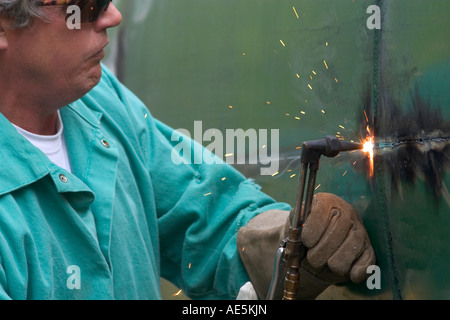 Sparks flying as welder uses torch to cut through large steel tank Stock Photo