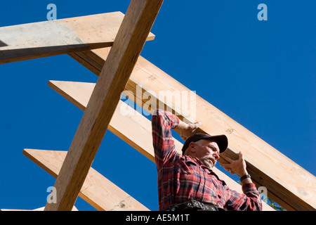 Carpenter lifting roof rafters into place on the ridge beam at a residential construction site Stock Photo