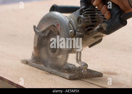 Carpenter using circular saw to cut plywood with sawdust flying Stock Photo