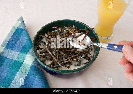 Hand spooning out nails from a bowl with milk at a breakfast table with orange juice - illustrates tough as nails Stock Photo