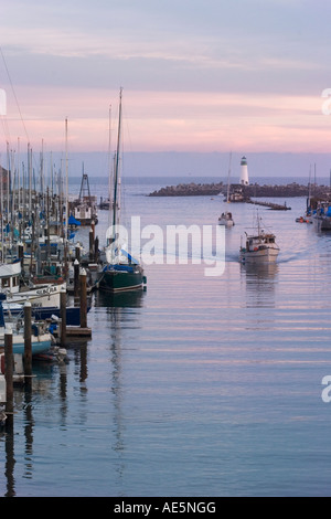 Fishing boat and sailboat pass by the Walton Lighthouse to arrive in the Santa Cruz Harbor at sunset Stock Photo