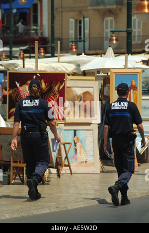 St Tropez waterfront street scene French police officers walk beside artists displays of paintings for sale Cote d Azur French Riviera South of France Stock Photo