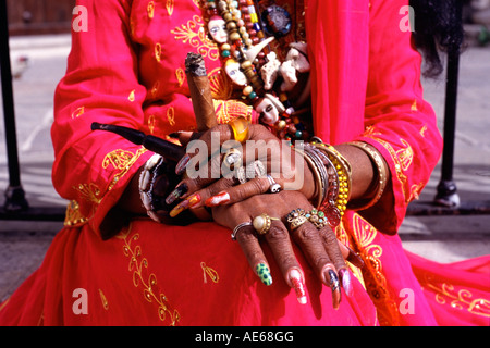 Hand of a Cuban woman wearing flanboyant clothes in Old Havana She is wearing many necklaces and is smoking a cigar on a pipe Stock Photo