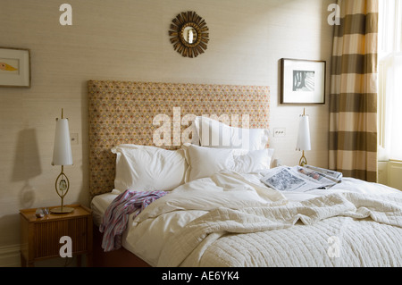 unmade double bed in bedroom with sunburst mirror Stock Photo