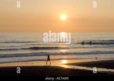 Cornwall, England: Women walking along the shoreline of Widemouth Beach in Cornwall at Sunset Stock Photo