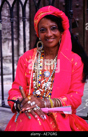 Cuban woman wearing flanboyant clothes in Old Havana She is wearing earings and many necklaces and is smoking a cigar on a pipe Stock Photo