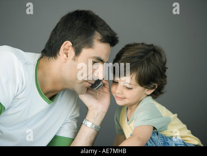 Man using cell phone, leaning toward son Stock Photo