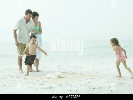 Family at the beach, children running around beach mat