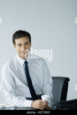 Businessman in office, holding cup and smiling at camera Stock Photo