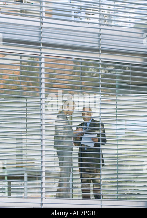Two business colleagues standing near glass wall, seen from exterior Stock Photo