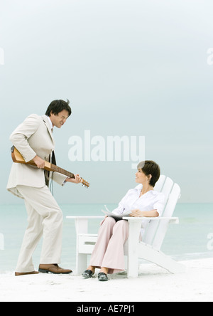 On beach, man in suit serenading woman sitting in deck chair Stock Photo