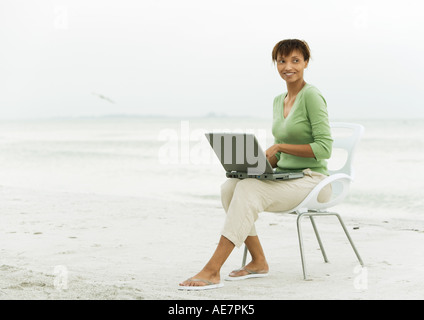 Woman on beach, sitting in chair using laptop Stock Photo