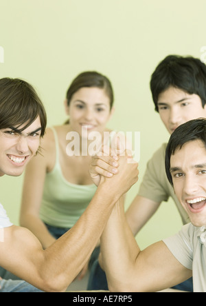 Two young men arm wrestling, friends in background Stock Photo