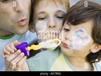 Father having fun with his two chiildren, blowing soap bubbles together, portrait, extreme close-up Stock Photo