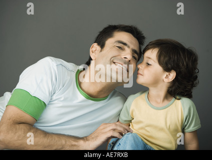 Father and son sitting side by side, child kissing his father's cheek, smiling, portrait Stock Photo