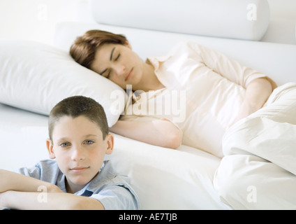 Boy sitting near sofa where mother is napping Stock Photo