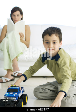 Boy playing with toy car while mother reads in background Stock Photo