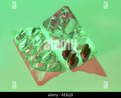 Blister pack with three dark red capsules Green lighting with hard shadow Stock Photo