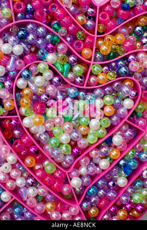 Colourful glass beads in a bright pink curved plastic heart shaped box Stock Photo