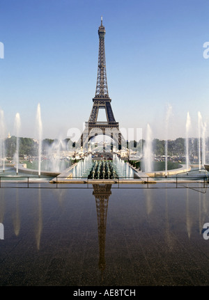 Symetrical composition of iconic & famous Eiffel tower landmark with water feature fountains reflected in still water blue sky day in Paris France Stock Photo