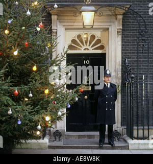 Metropolitan Police officer evening night duty standing outside iconic front door of number ten 10 Downing Street beside illuminated Christmas tree UK Stock Photo