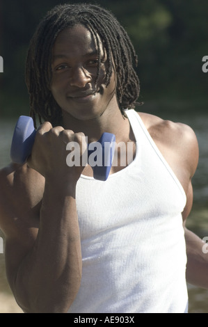 An fit healthy youthful handsome African American man exercising in a white tank top outside with small barbell weights. Stock Photo