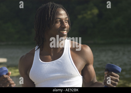 An fit healthy youthful handsome African American man exercising in a white tank top outside with small barbell weights. Stock Photo