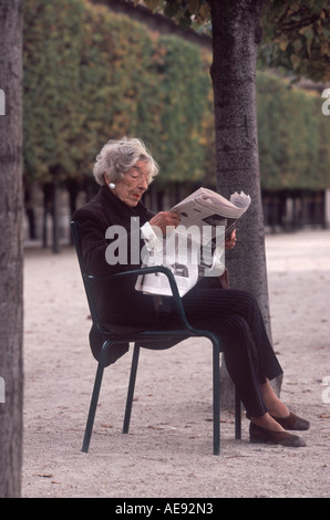 Mature woman reading Le Figaro newspaper sitting outside in the Jardin du Palais Royal, Paris, France Stock Photo