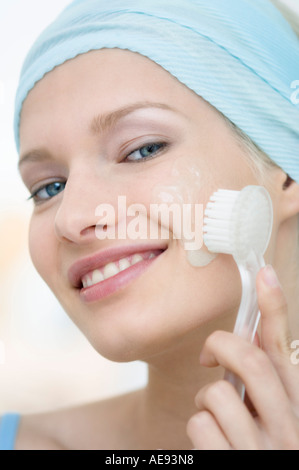 Young Woman face looking at the camera, cleaning her cheeks with a brush, close-up (studio) Stock Photo
