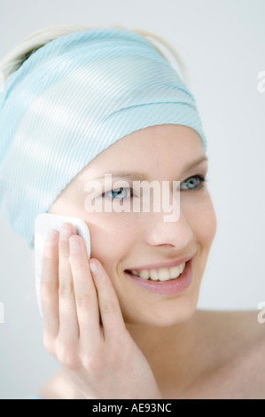 Young Woman face with make up, holding a cleansing cotton on her cheek (studio) Stock Photo