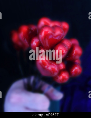 Bouquet of shiny red hearts on stems in a man's hand against a dark blue background. Stock Photo