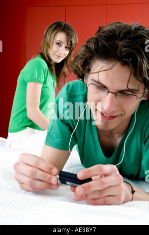 Young man lying on bed,  MP3 player, woman sitting in background Stock Photo