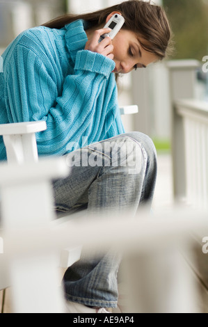 Young woman using mobile phone, sitting on a chair, outdoors Stock Photo
