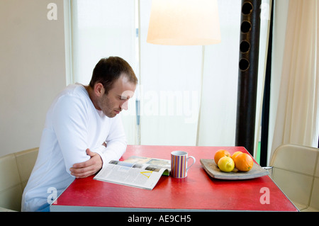 Man sitting in the kitchen, reading a magazine Stock Photo