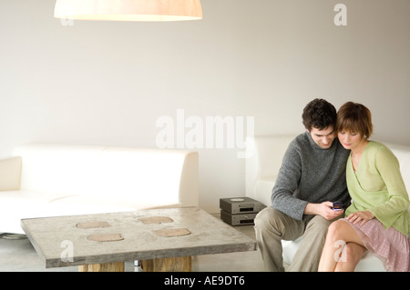 Couple sitting on a sofa in living-room,using mobile phone Stock Photo