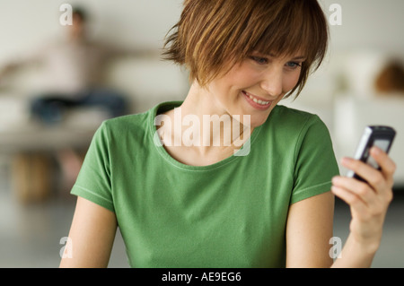 Smiling woman holding mobile phone, man in the background Stock Photo